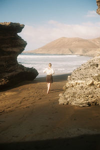 Man standing on rock by sea against sky
