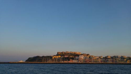 Sea by buildings against clear blue sky