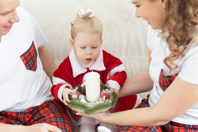 Smiling man looking at woman giving christmas candle to daughter at home