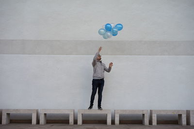 Man reaching balloons while standing on bench outdoors