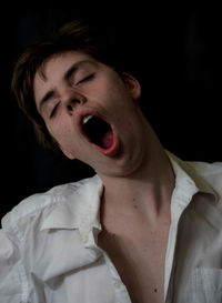 Close-up of teenage boy yawning against black background