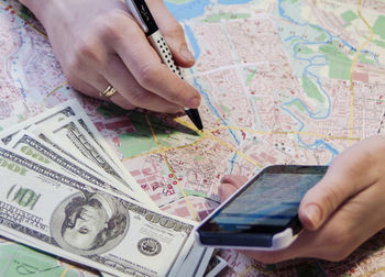 Cropped hands of woman using phone with paper currency on map at table