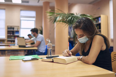 A girl in a mask studying in the library keeping a safe distance