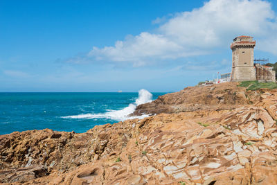 Lighthouse on beach by sea against sky