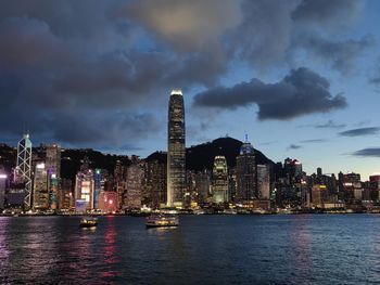 Illuminated buildings by river against sky at dusk