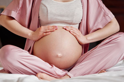 Midsection of pregnant woman touching belly sitting on bed