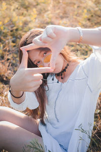 Portrait of woman making finger frame on field