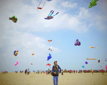 Woman standing on field with kites flying against sky