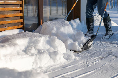 A man in rubber boots with a snow shovel cleans the snow from the terrace of the house