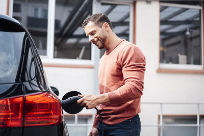 Smiling man charging electric car outside building