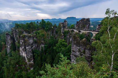 View of trees on landscape against cloudy sky