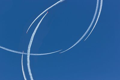 Low angle view of vapor trails against clear blue sky