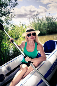 Portrait of mid adult woman wearing sunglasses canoeing on lake against cloudy sky