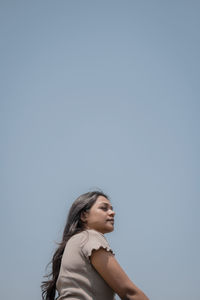 Young woman looking away against clear sky