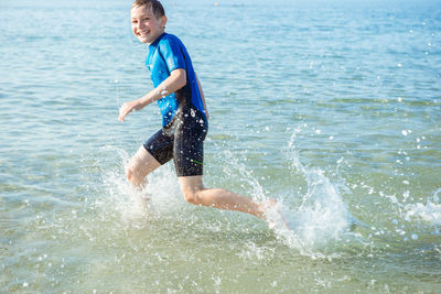 Full length of boy splashing water in sea