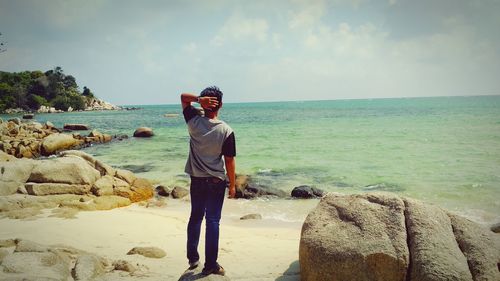 Full length of man standing on rock at beach against sky