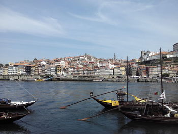 Sailboats moored at harbor by buildings in city against sky