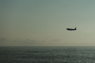 The silhouette of the plane flies against the background of the sky and the sea