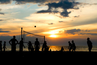 Silhouette people playing on beach against sky during sunset