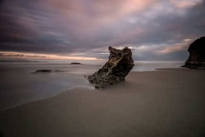 Rocks on beach against sky during sunset