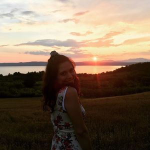 Woman standing on field against sky during sunset