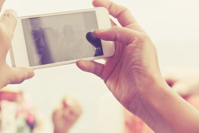 Close-up of man photographing through mobile phone against sky at beach