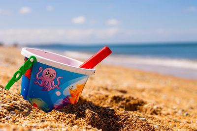 A child's bucket for playing in the sandbox with a shovel stands on the shore of the blue sea