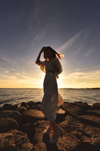 Side view of woman standing at beach against sky during sunset