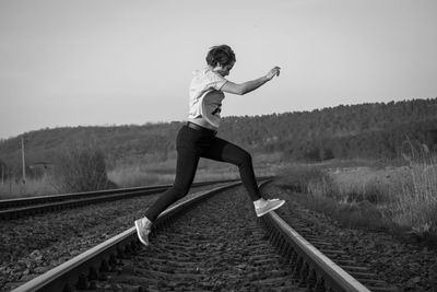 Full length of young woman jumping over railroad tracks against clear sky