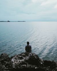 Rear view of man sitting by sea against sky