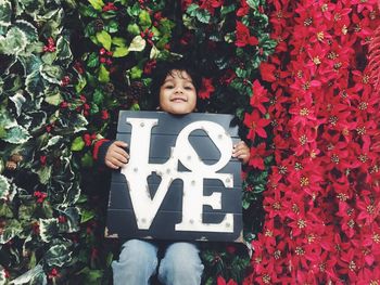 Portrait of boy holding love text by plants