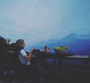 Woman sitting on chair at table against sky