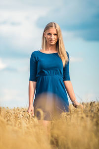 Portrait of smiling young woman standing on field against sky