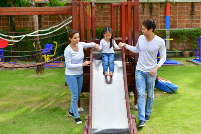 Girl holding hands of father and mother while sliding on slide at park