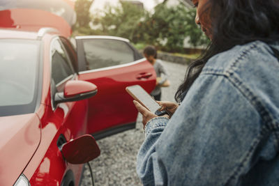 Woman using smart phone next to electric car