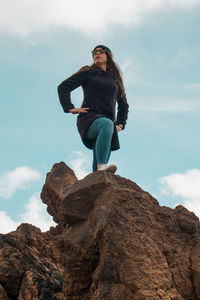 Low angle view of woman standing on rock against sky