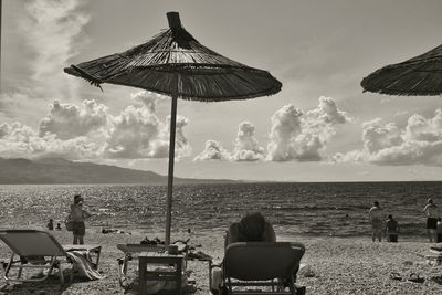 People relaxing on table at beach against sky
