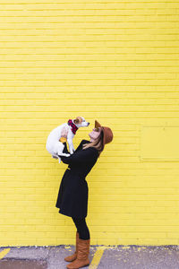 Side view of young woman photographing against yellow wall