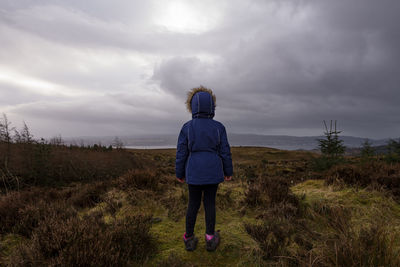 Rear view of boy walking on field against sky