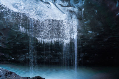 Clean water falling from fragile transparent icicles into blue stream inside ice cave in vatnajokull glacier in iceland
