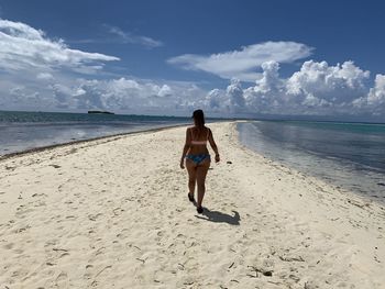 Rear view of woman walking on beach against sky