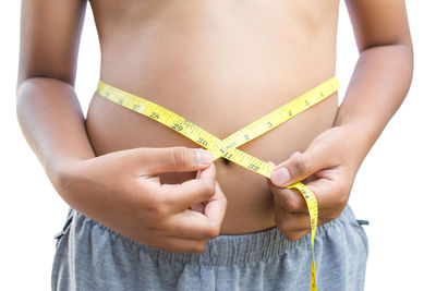 Midsection of shirtless boy measuring waist against white background