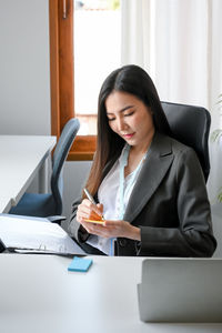 Businesswoman writing on adhesive note at office