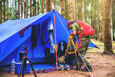 Man standing by tent against trees in forest