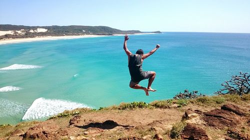 Full length of man jumping on cliff against sea