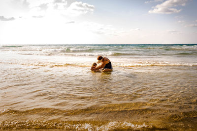 Couple sitting on beach against sky