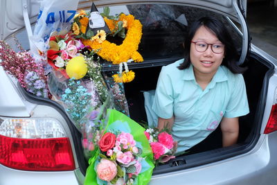 Smiling young woman with bouquets sitting in car trunk