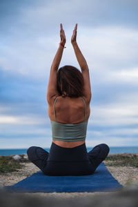Rear view of woman exercising at beach against sky