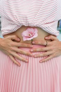 Midsection of woman holding pink flower