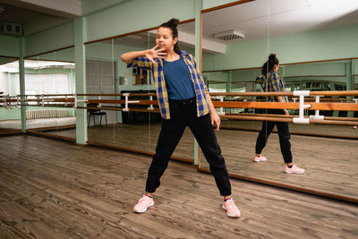 Pretty young woman showing dance move while engaged in contemporary dance alone in choreography hall